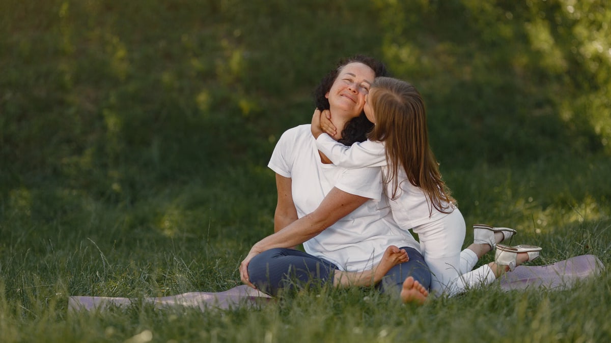 A joyful moment between mother and daughter hugging on a grassy field.