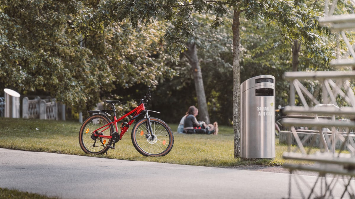 A red bicycle parked in a lush, sunny park with people relaxing nearby in Graz, Austria.